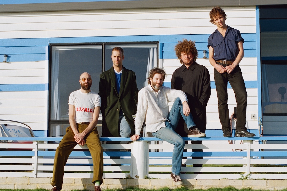 Psychedelic rock band Pond posing outside a blue and white weatherboard house on a sunny day.